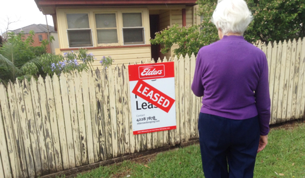 Older woman standing in front of a 'leased' sign