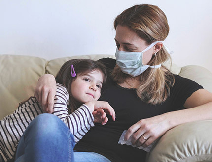 A mother and child sitting on a couch. The mother is wearing a face mask.