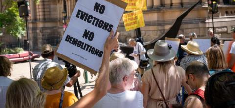 A woman holds a sign saying no evictions no demolitions with other protestors outside Sydney Town Hall