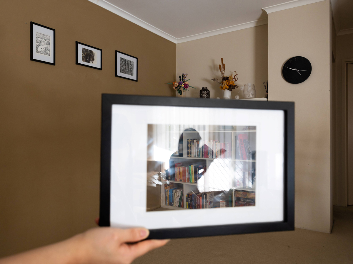 A hand holding a picture with a reflection of a person reading in a living room