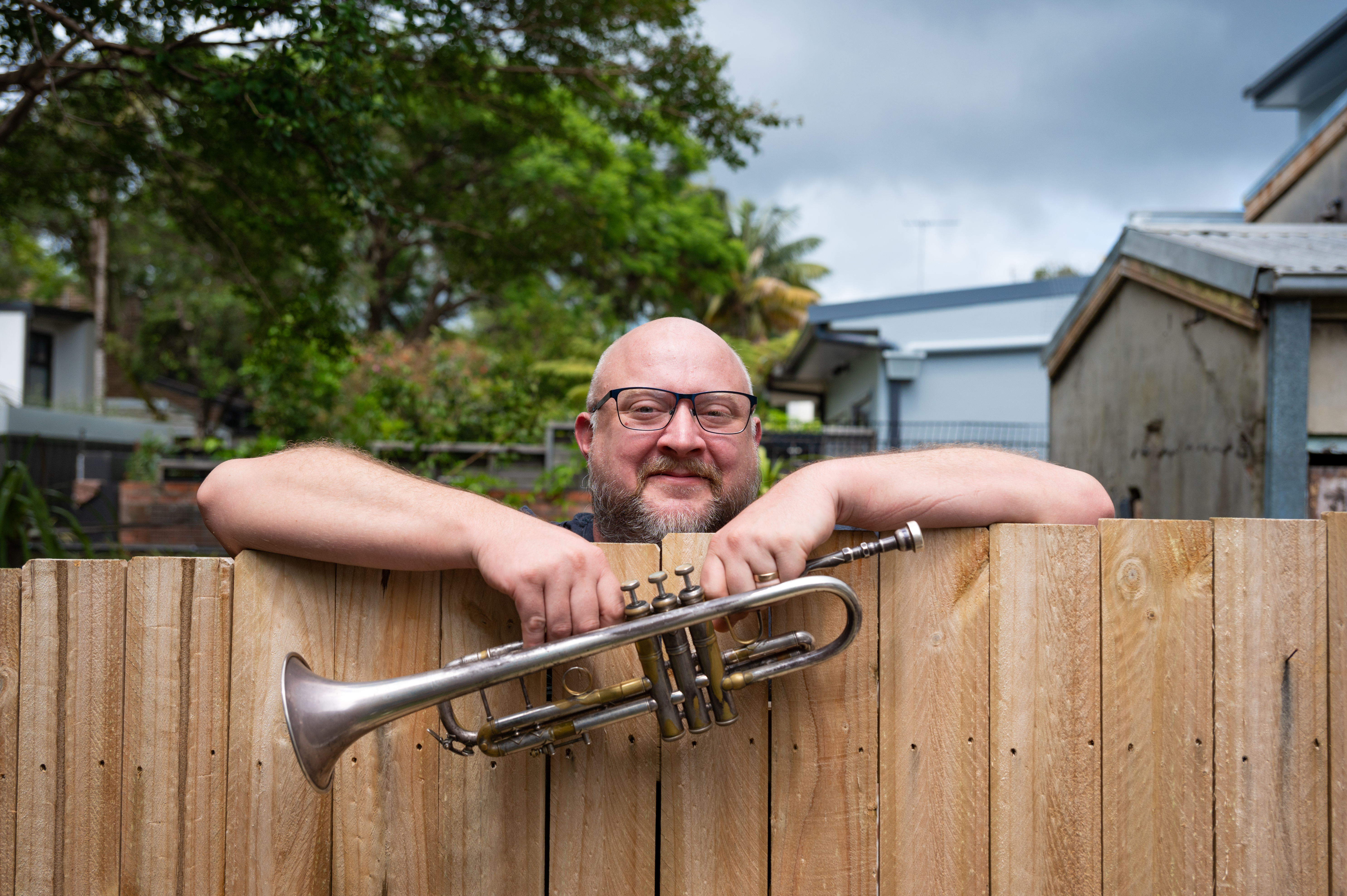 A man looking over a fence, holding a trumpet